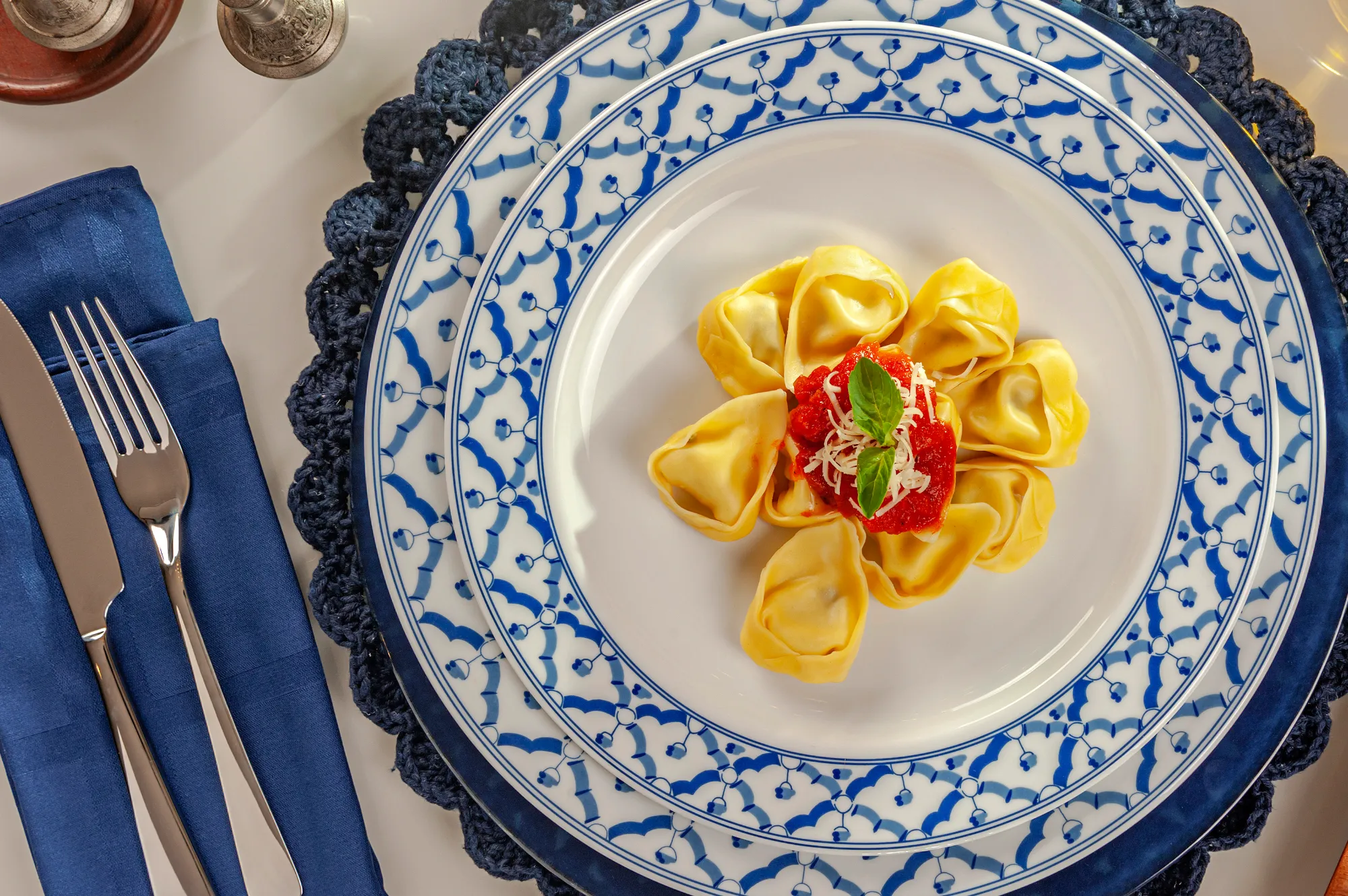 Tortellini com molho ao sugo, queijo ralado e manjericão em prato de porcelana azul e branca