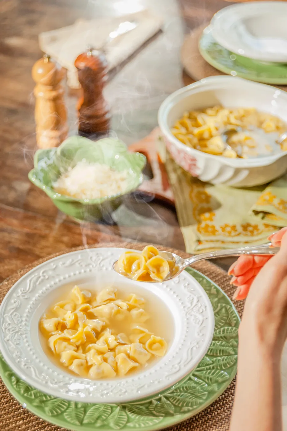 Cappelletti em caldo quente servidos na colher, com queijo ralado ao fundo