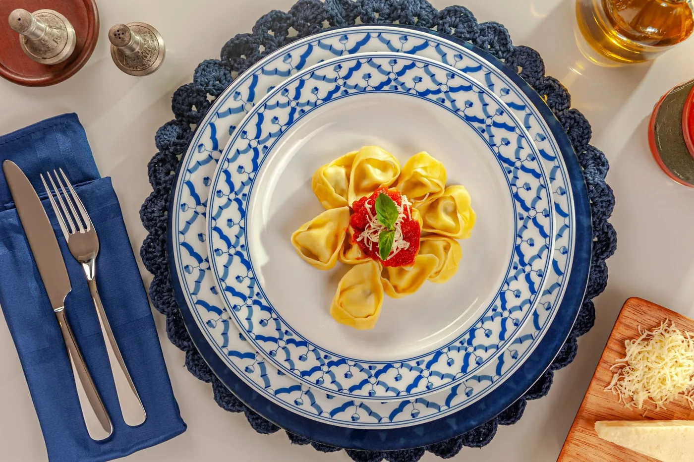 Tortelloni com molho ao sugo, queijo ralado e manjericão em prato de porcelana azul e branca